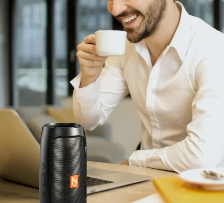 Man working at a home office desk with the WallaSound speaker beside his laptop